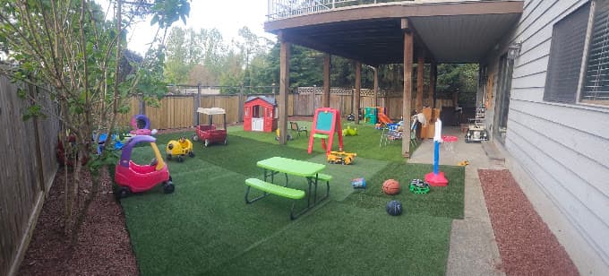 Covered backyard play area with a picnic table, playhouse, and outdoor toys